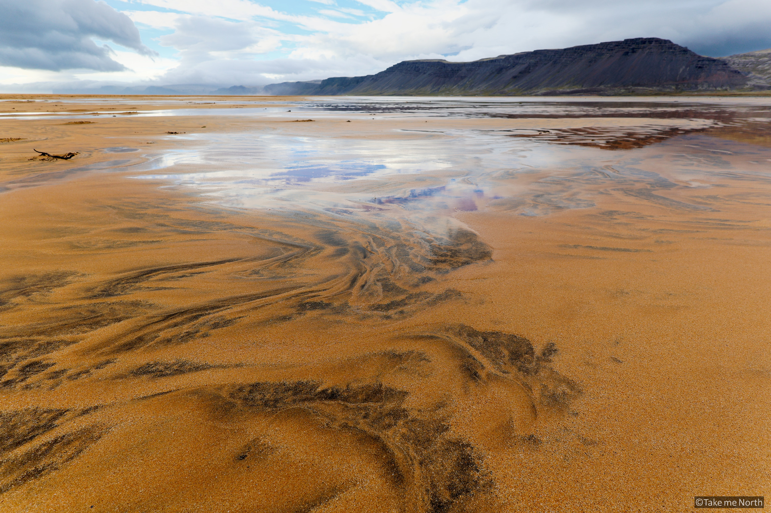Shallow pools left by the ebbing tide mirror the sky above.